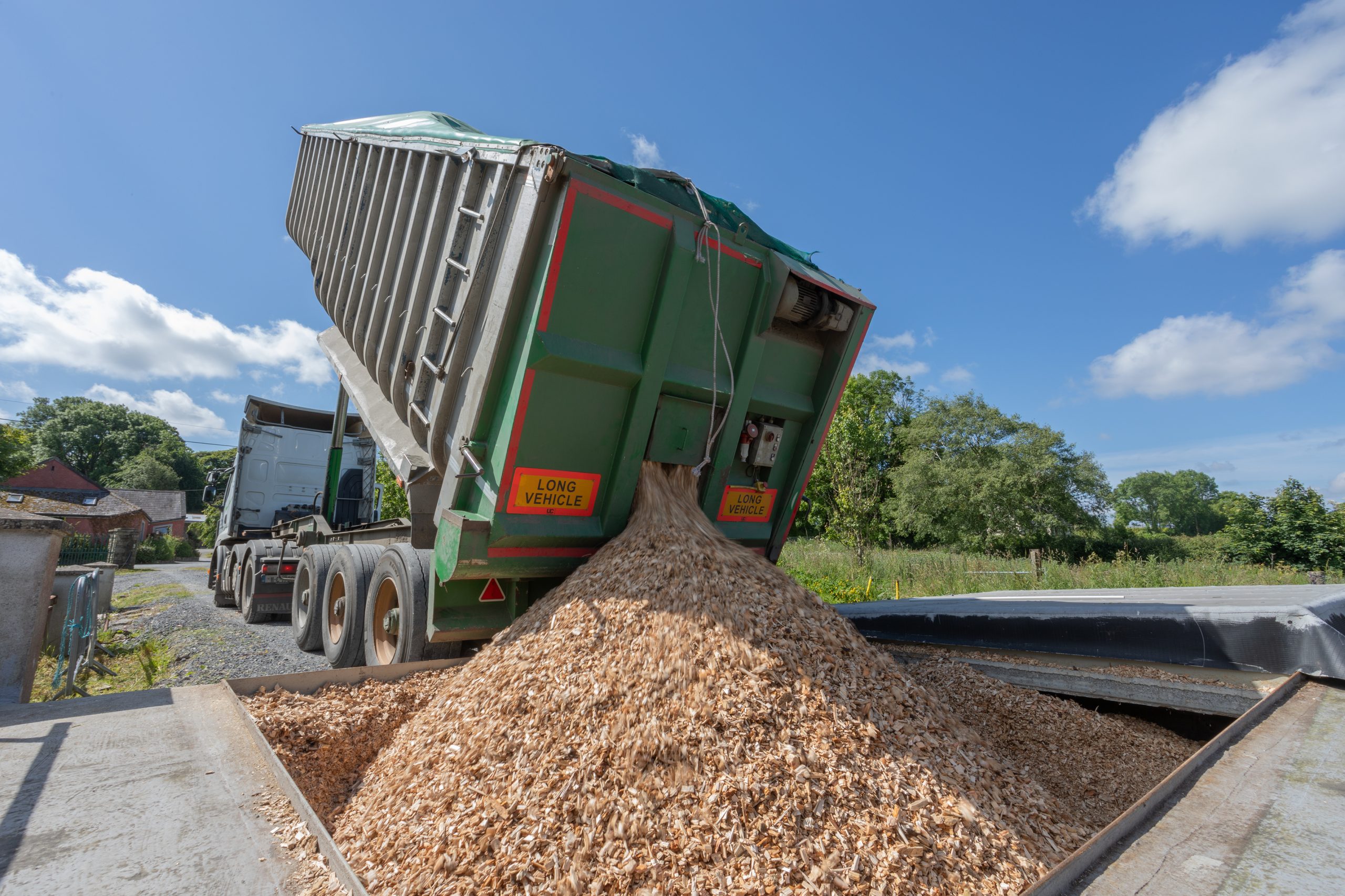 Wood chip delivery truck unloading renewable biomass fuel at a commercial site for use in heating systems or landscaping