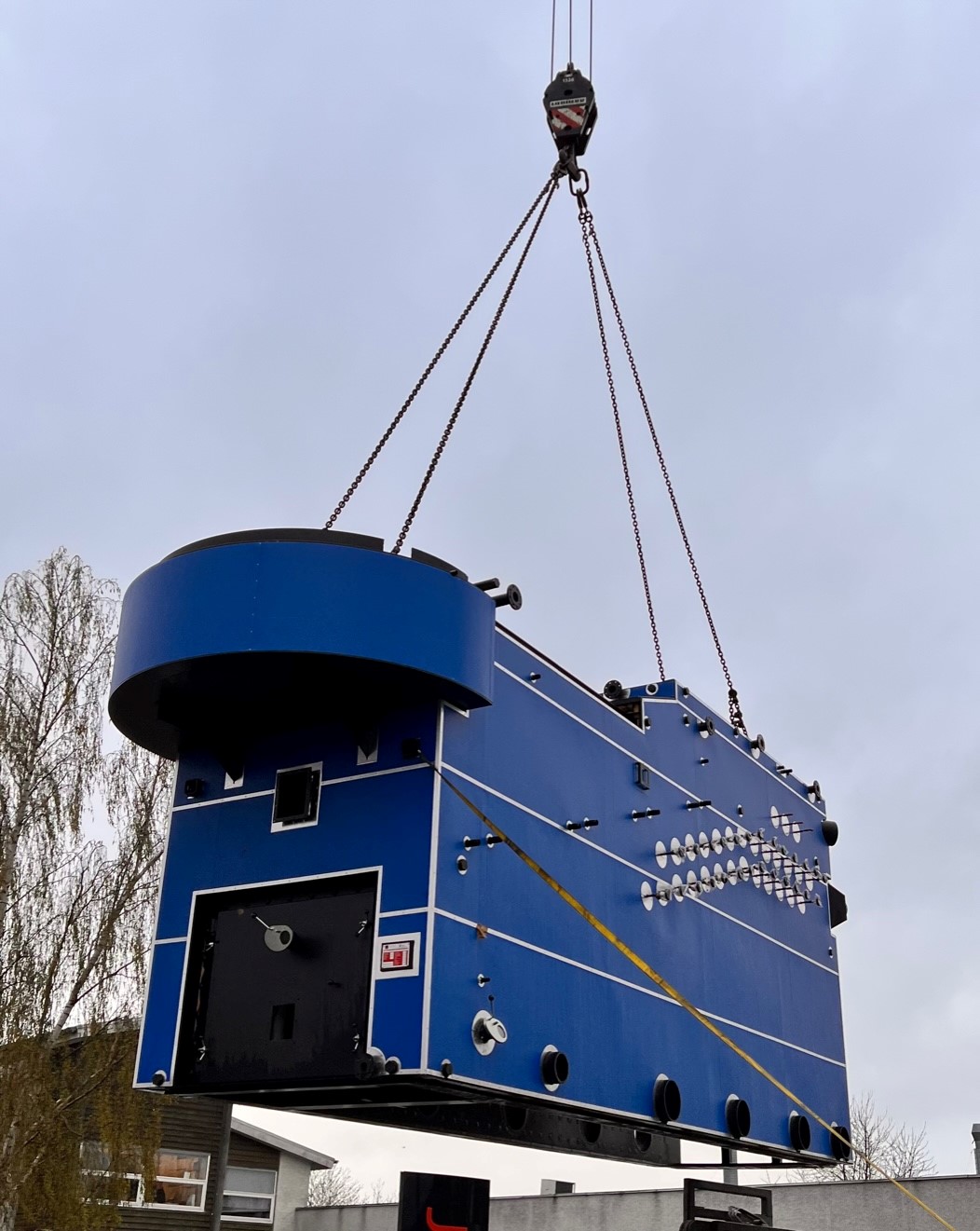 Industrial biomass boiler being installed in a large building, with visible fuel storage, pipework, and the control panel setup