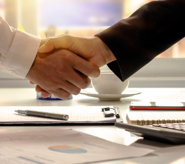 Two individuals shaking hands or signing a document to finalize a business deal or agreement, symbolizing partnership and mutual agreement